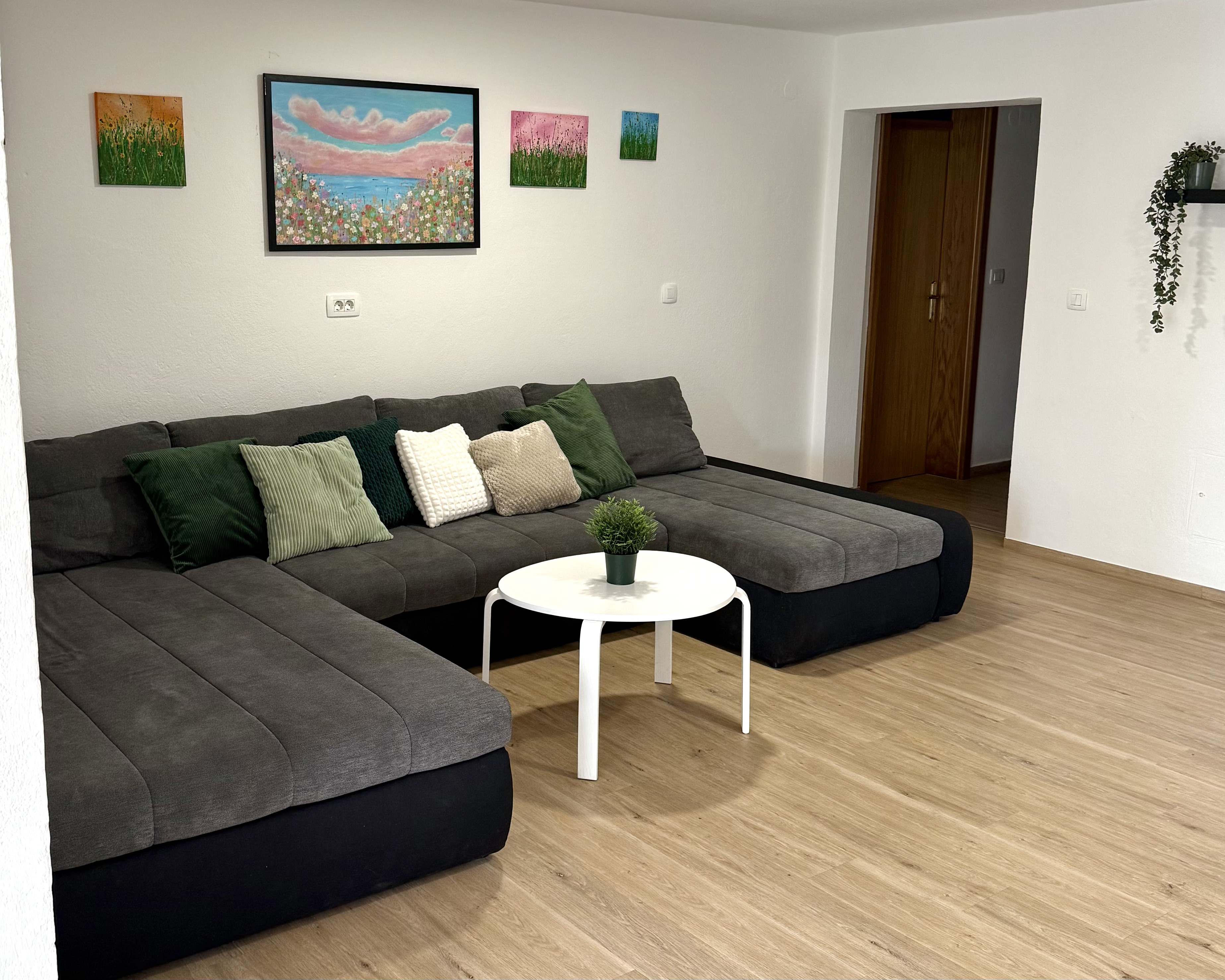 Living room with large corner sofa, colourful artwork and indoor plants