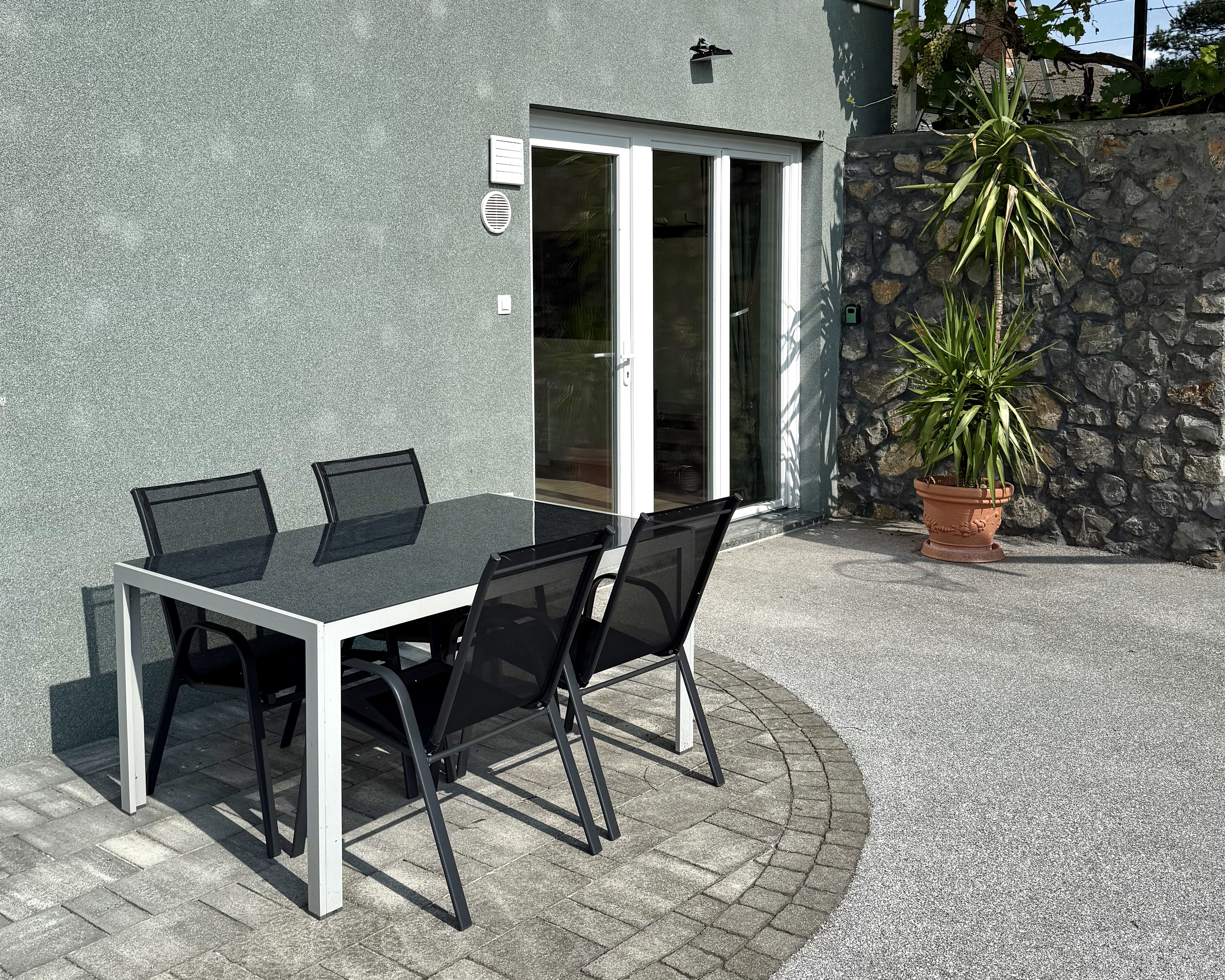 Outdoor terrace with dining table and chairs, stone wall and tropical plant